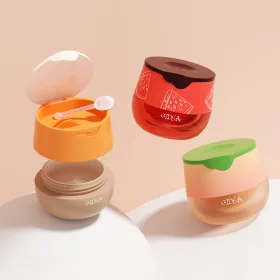 three GIDEA fruit-themed cosmetic jars (lip balm or face cream), featuring watermelon, orange, and avocado cap designs, with one jar open showing the included applicator spoon